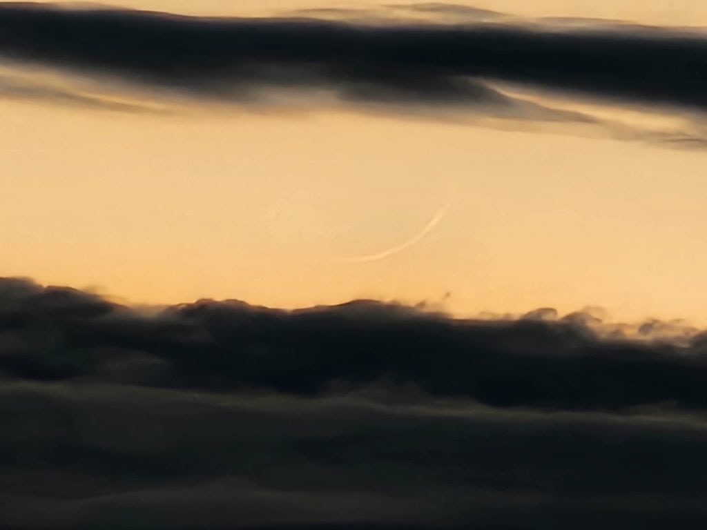 A crescent moon is seen in the sky above clouds.