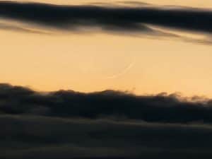 A crescent moon is seen in the sky above clouds.