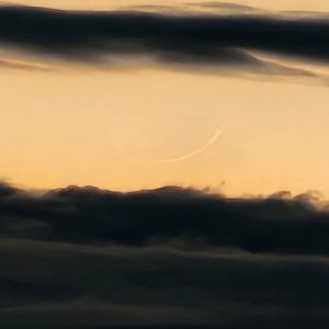 A crescent moon is seen in the sky above clouds.